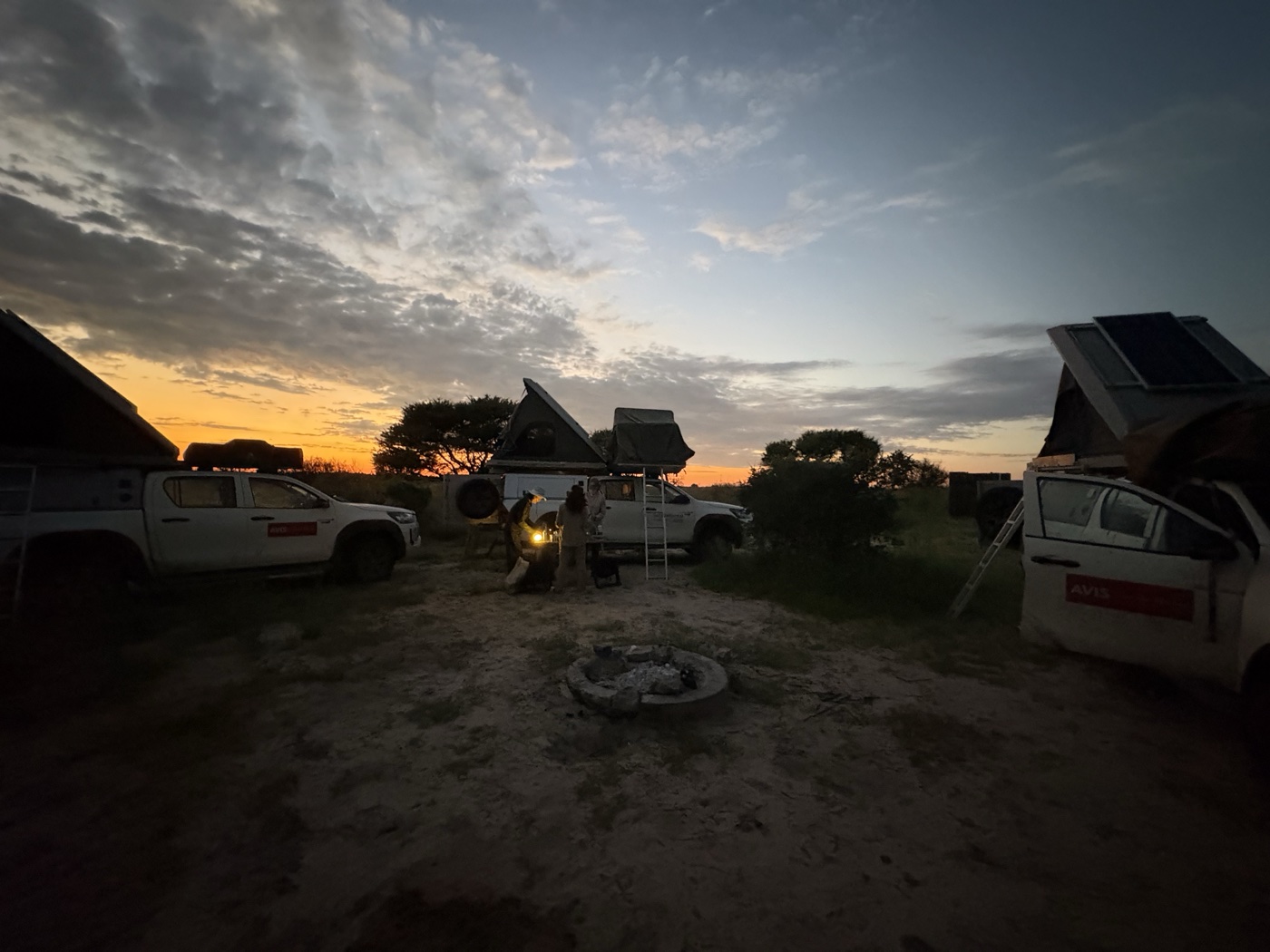 Camp at dusk in Botswana — three AVIS Hiluxes with rooftop tents around a campfire